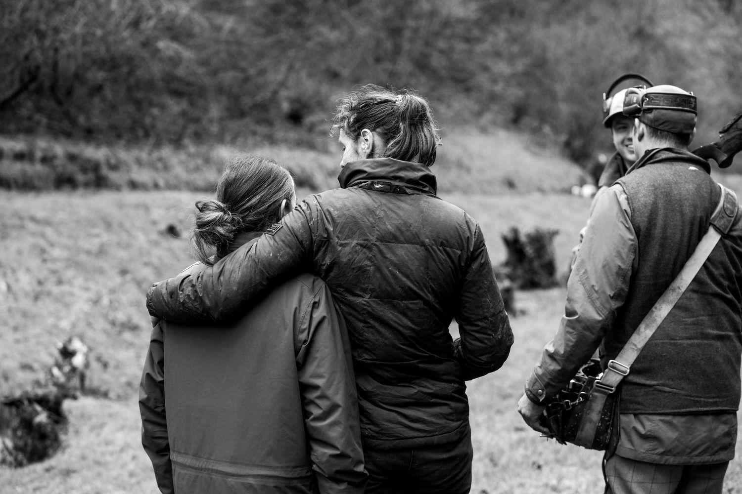 Three people in winter coats standing together outdoors in a black and white nature scene.