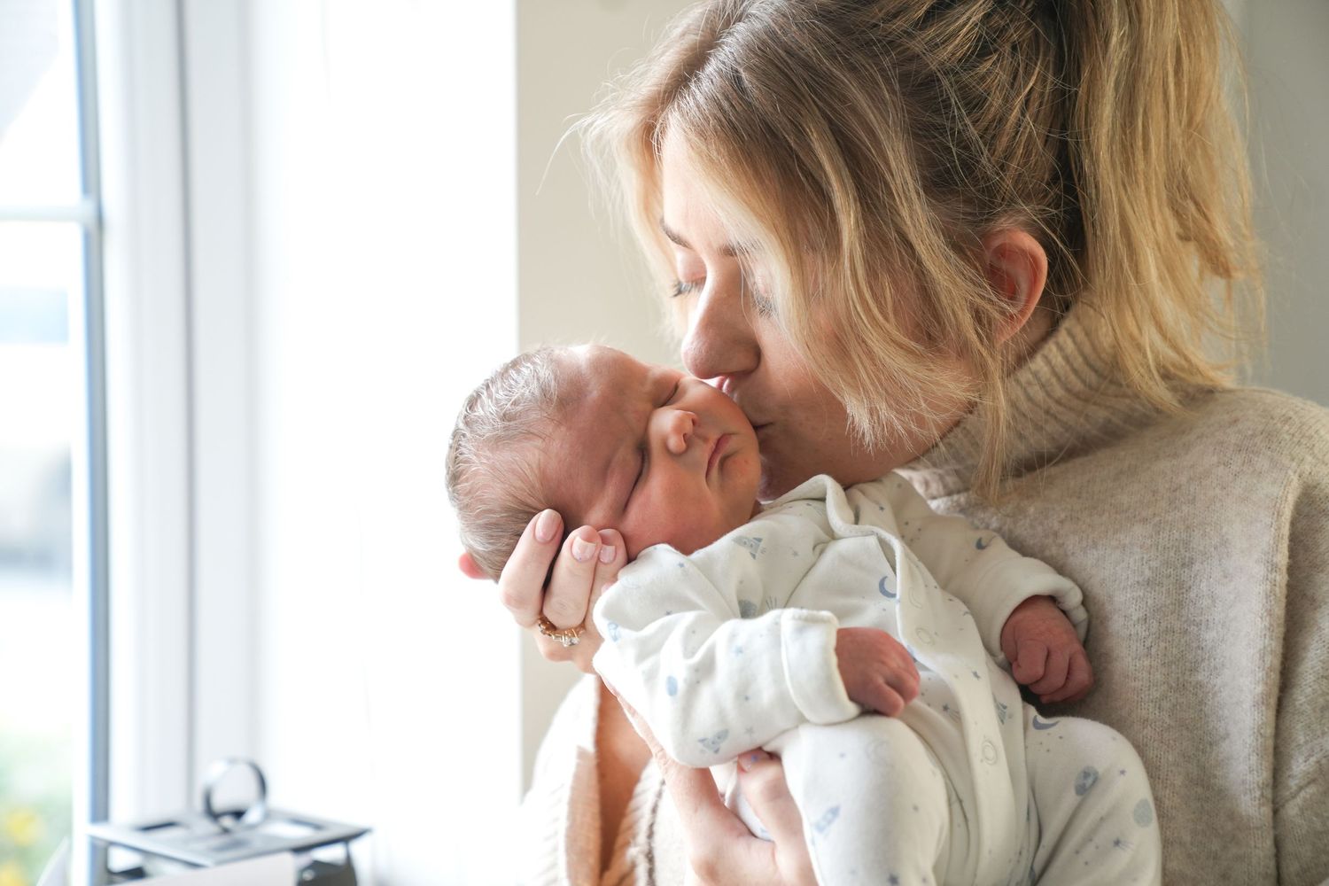 A tender moment between parent and newborn baby by a bright window.