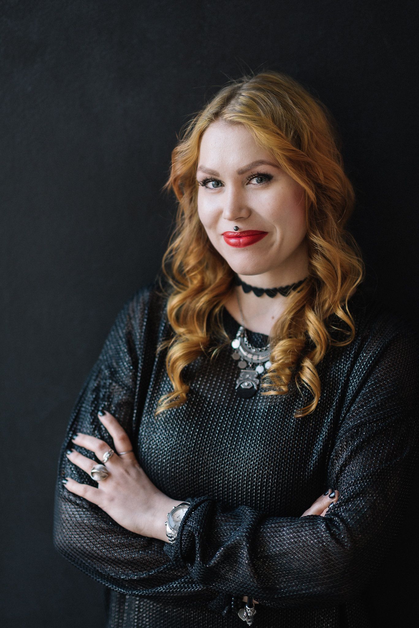 Stylish portrait featuring knit sweater, statement necklace and wavy copper hair against dark background.