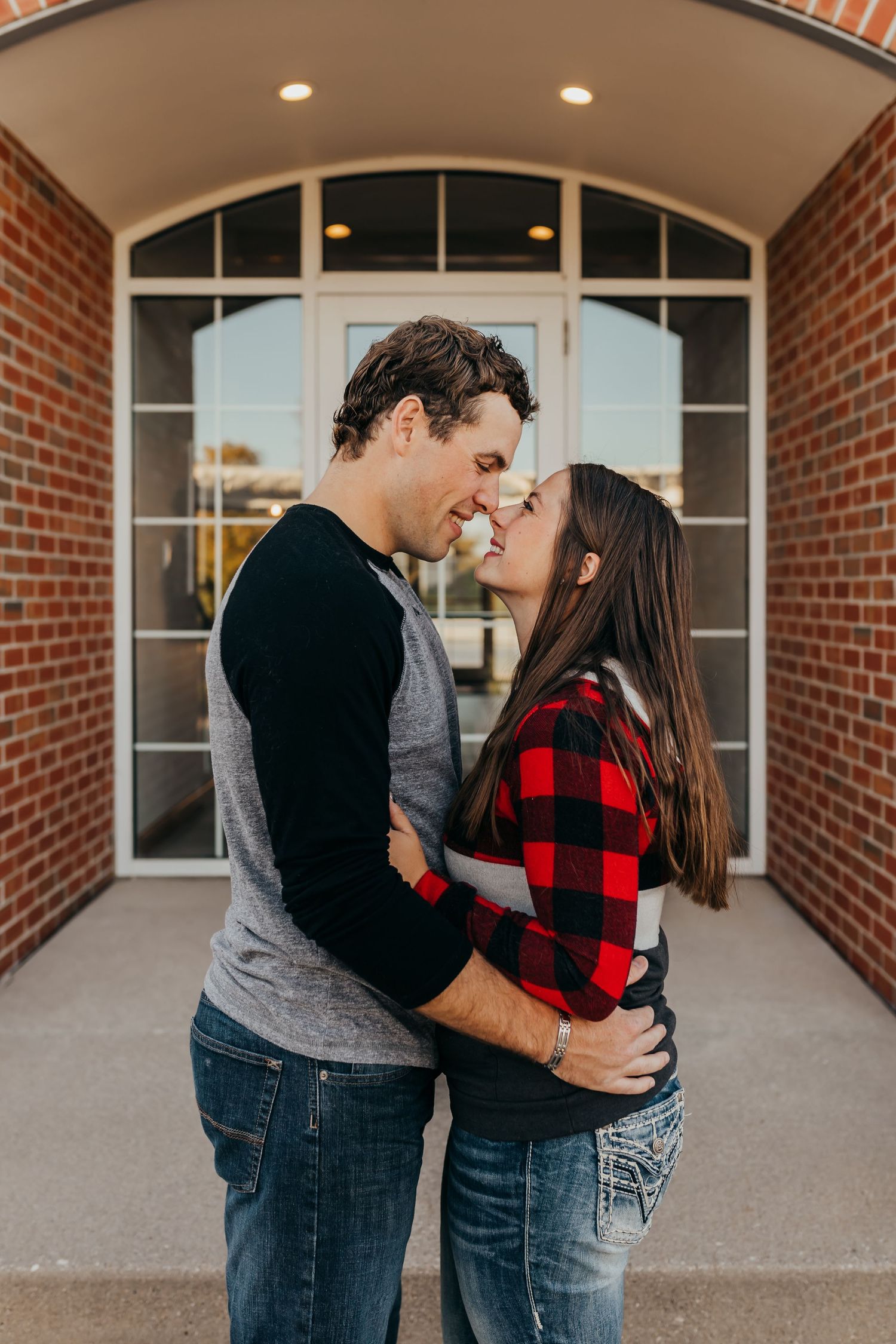 A couple embracing in a romantic moment outside a brick building with arched windows.