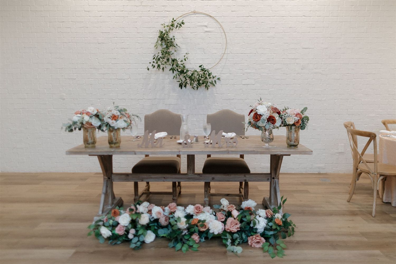 Elegant wedding table setup with greenery hoop decor and floral arrangements on rustic wooden table.