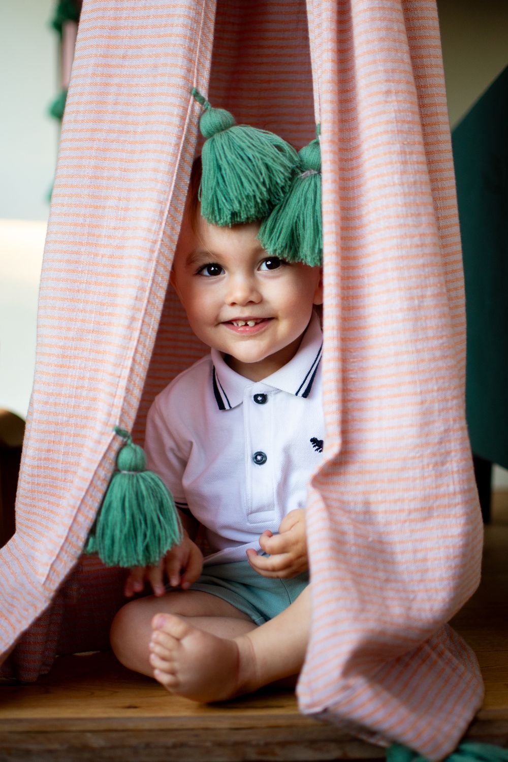 A little boy playing with curtains at home in Cambridge, UK
