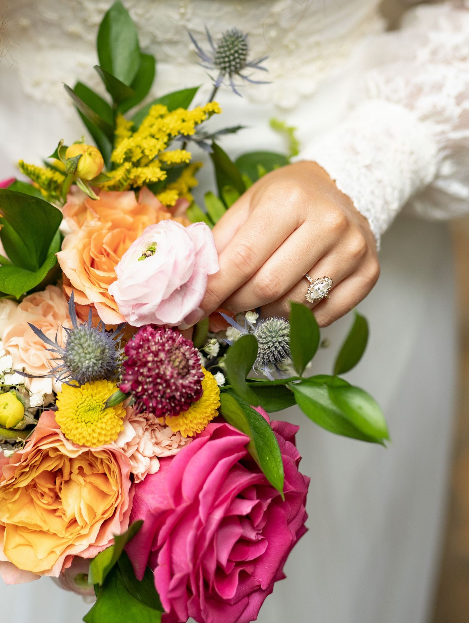Vibrant wedding bouquet with pink roses, yellow flowers, and orange carnations against white fabric.