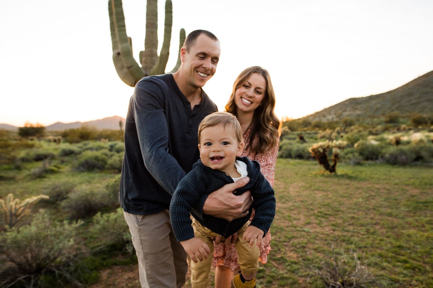Beautiful lush green desert view with this playful family of three laughing for a portrait with their baby.