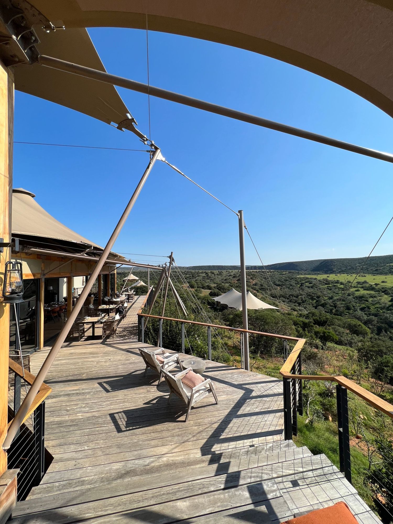 Curved wooden deck with canvas shade sails overlooking scenic valley landscape.