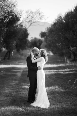 Black and white wedding portrait of couple embracing on a tree-lined path.
