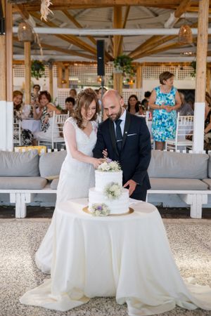 A wedding couple prepares to cut their white tiered cake at an outdoor reception venue.