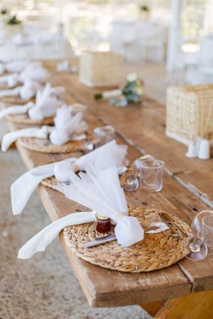 Rustic wedding place settings with woven chargers and white napkins on wooden tables.
