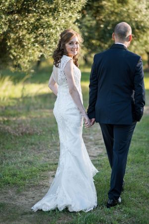 Classic wedding portrait of couple in elegant attire walking along a garden path.