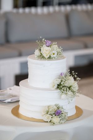 An elegant two-tier white wedding cake decorated with fresh roses and baby's breath.