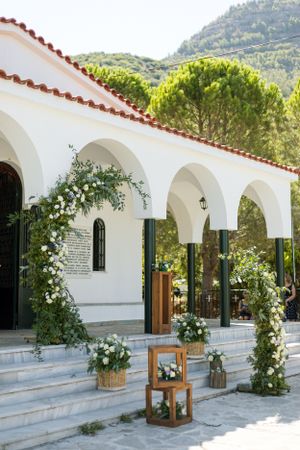 White Mediterranean-style church entrance decorated with floral arches and lanterns for a wedding.