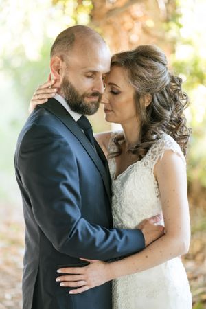 Intimate moment between newlyweds sharing a tender embrace outdoors in natural sunlight.