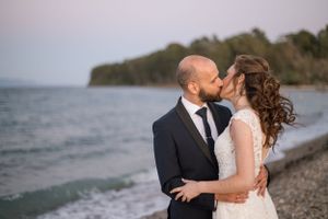 Newlyweds share an intimate moment on a beach with trees and mountains in the background.