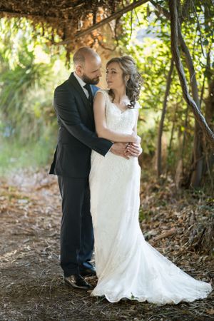 Happy couple sharing a joyful moment on a scenic woodland path in their wedding attire.