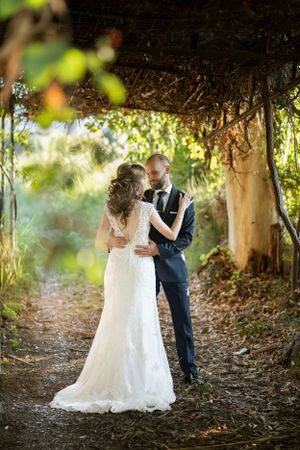 Wedding couple embracing under a natural garden arbor with dappled sunlight.