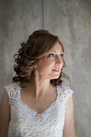 Elegant bridal portrait against textured grey wall with soft natural lighting.