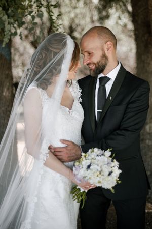 An intimate wedding moment captured under trees with white floral bouquet.
