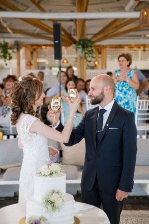 Newlyweds share a toast with champagne glasses during their outdoor reception celebration.