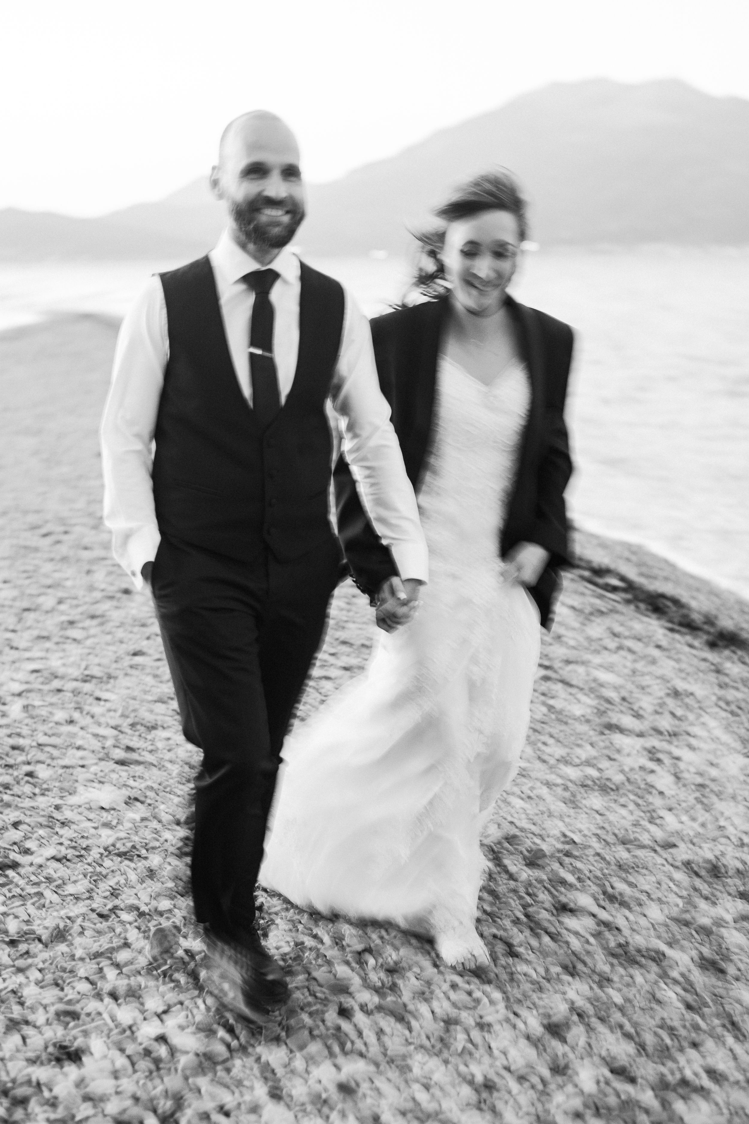 Black and white photo of a couple walking hand in hand along a beach shore.