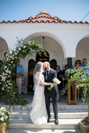 A wedding exit through a Mediterranean-style church archway decorated with white floral arrangements.