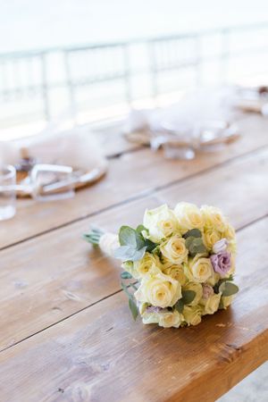 A delicate bouquet of cream roses and eucalyptus leaves rests on a rustic wooden table.