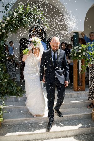 Newlyweds exit their ceremony under a shower of white confetti and floral decorations.