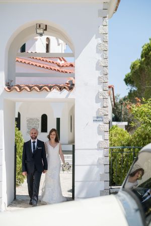 A wedding couple stands in a Mediterranean-style archway with white walls and terracotta roof tiles.