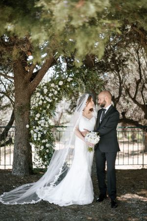 A romantic wedding portrait under a blooming tree arch with flowing veil.