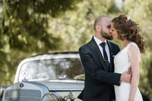 A tender moment captured between newlyweds beside a vintage Mercedes car.