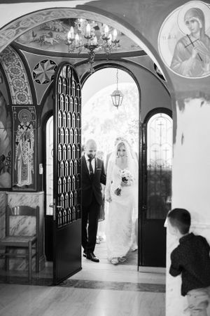 A black and white photograph of a wedding ceremony entrance in an ornate Orthodox church.