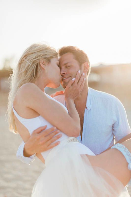 Un couple romantique s’enlace et s’embrasse dans la lumière dorée du coucher du soleil sur la plage.