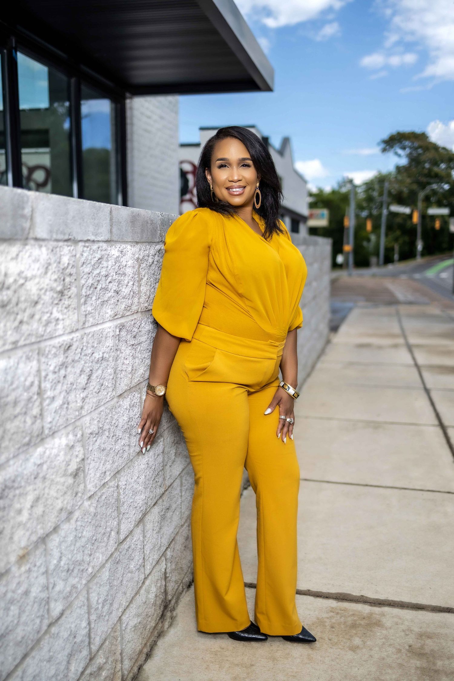 Bright yellow outfit worn against white stone wall on sunny sidewalk with trees in background.