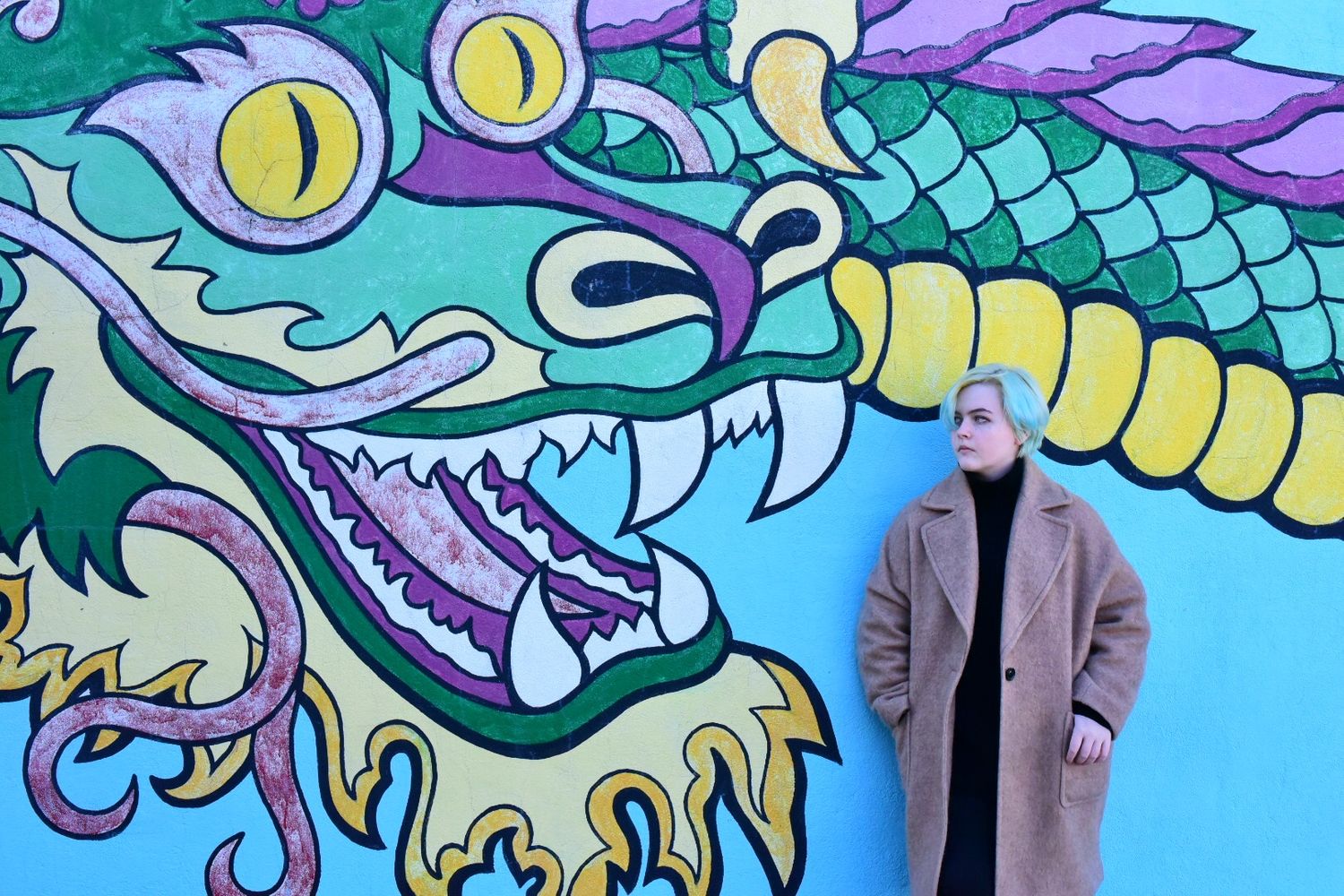 Colorful dragon mural painted on bright blue wall with person standing beside it.