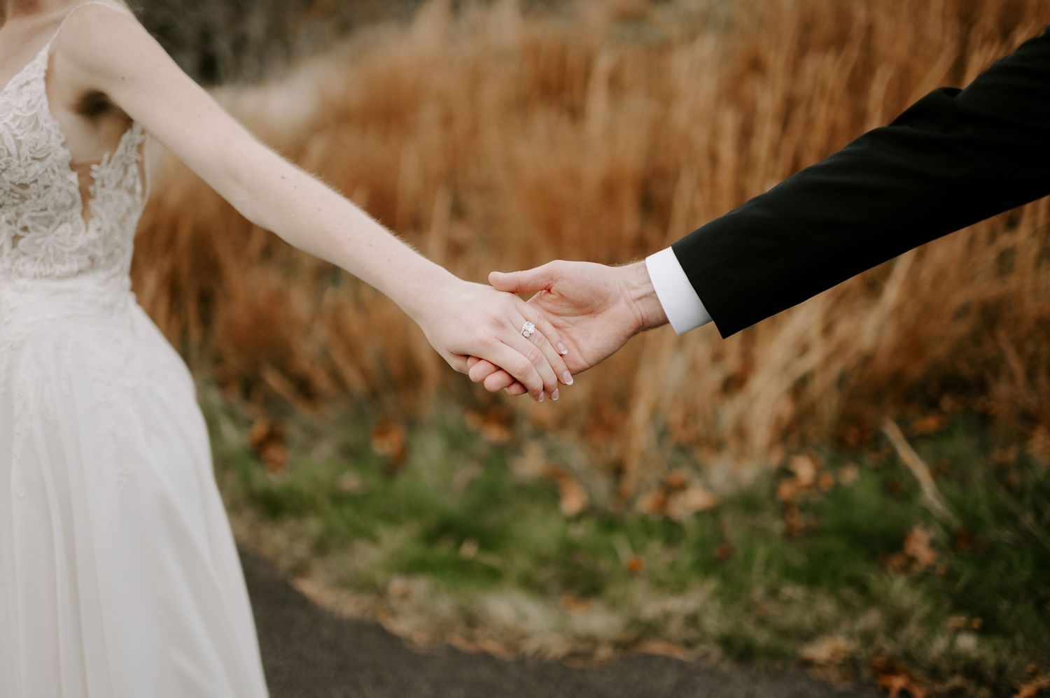 Close-up of newlyweds holding hands with wedding attire visible against fall foliage.