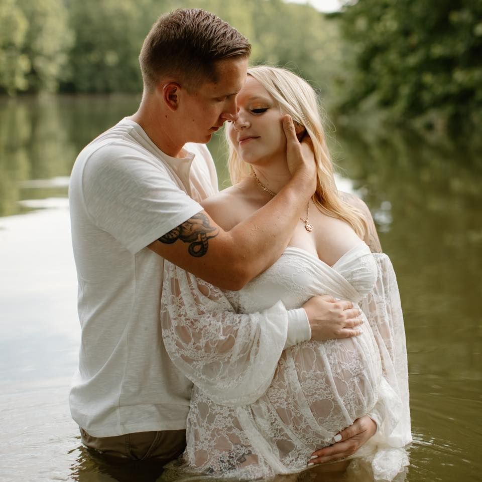 Romantic couple shares intimate moment in white attire by tranquil water.