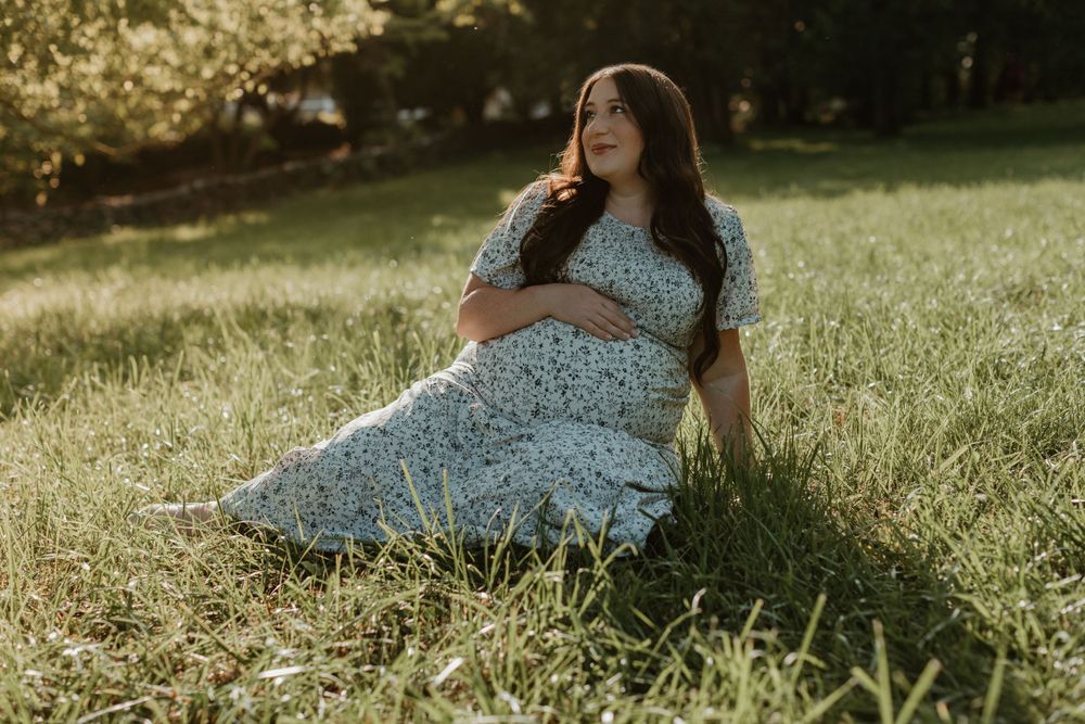Woman in floral dress relaxes on grass during golden hour photoshoot.
