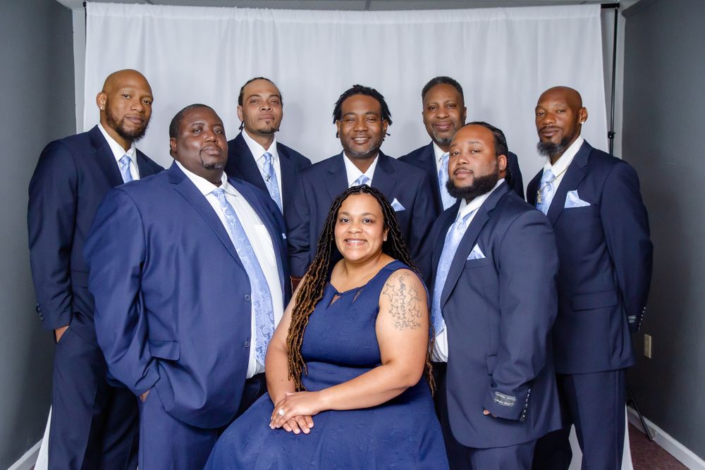 Formal group photo of wedding party in navy blue attire against grey studio background.