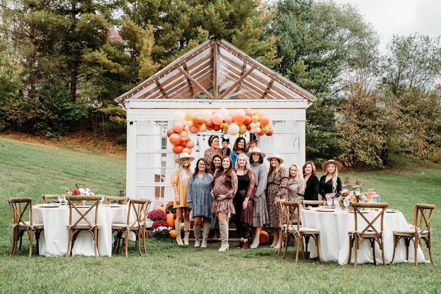White wooden structure decorated with autumn florals and cross-back chairs for outdoor event.