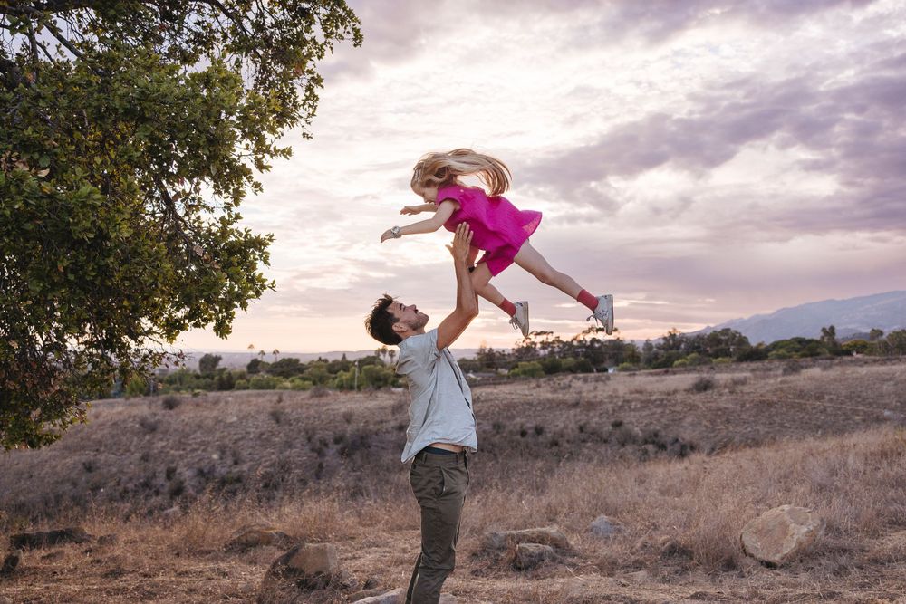 A playful moment of lifting and spinning captured against a dramatic sunset sky.