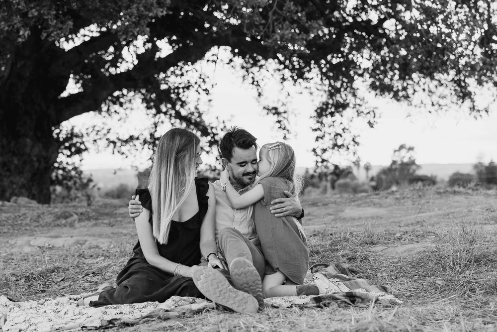 A black and white photo of a family sharing a joyful moment under a large tree.