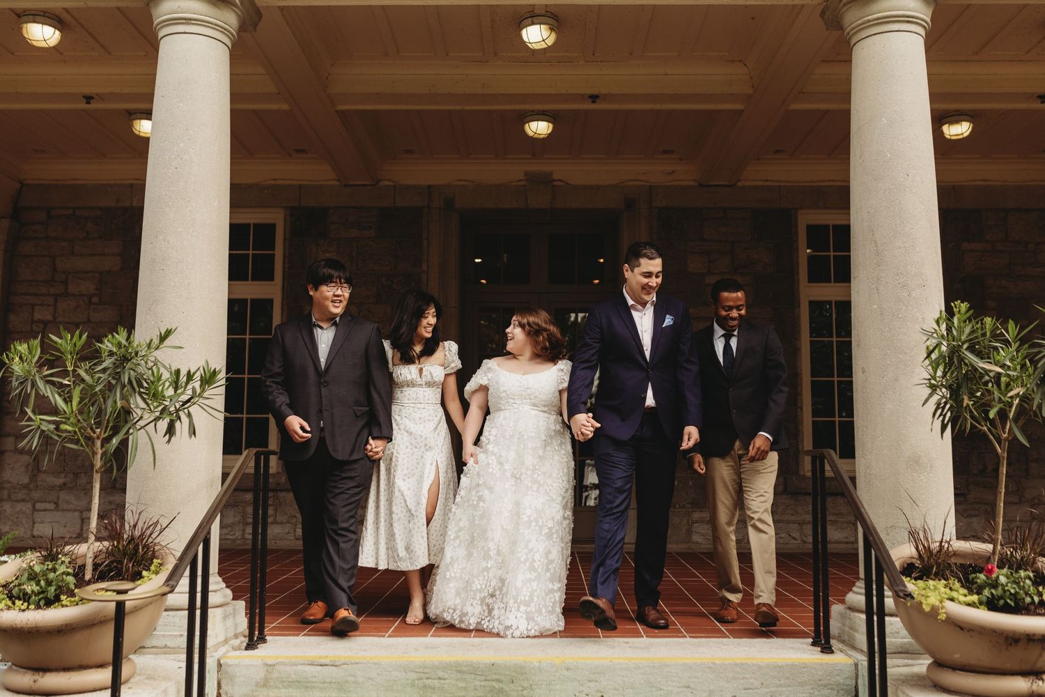 Wedding party poses on red-carpeted steps between classic white columns.