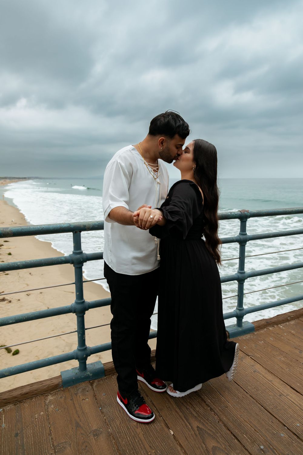 A couple shares an intimate moment on a pier overlooking the ocean under dramatic cloudy skies.