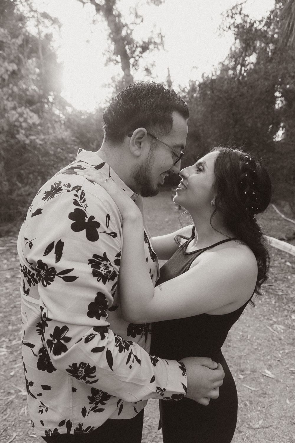 A couple in black and floral print sharing an intimate embrace on a forest path.