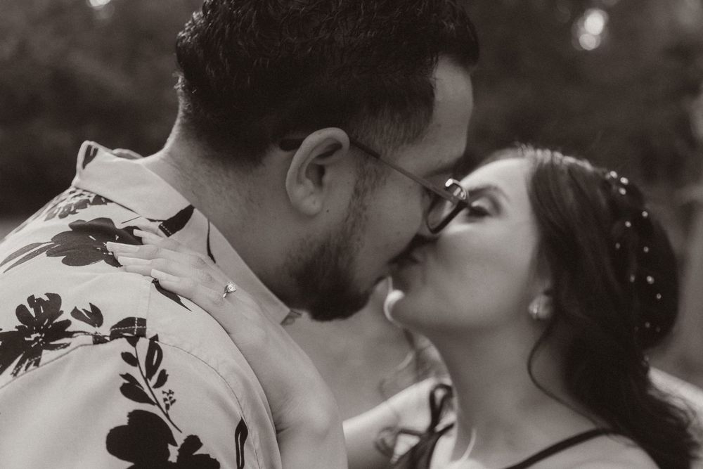 A black and white romantic portrait showing a couple sharing a kiss in nature.