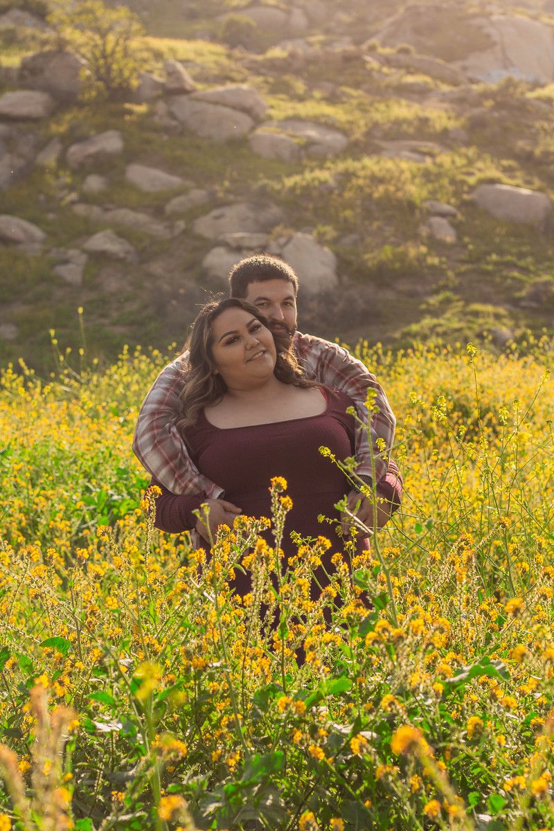 Couple shares intimate moment surrounded by golden wildflowers and rocky hillside.