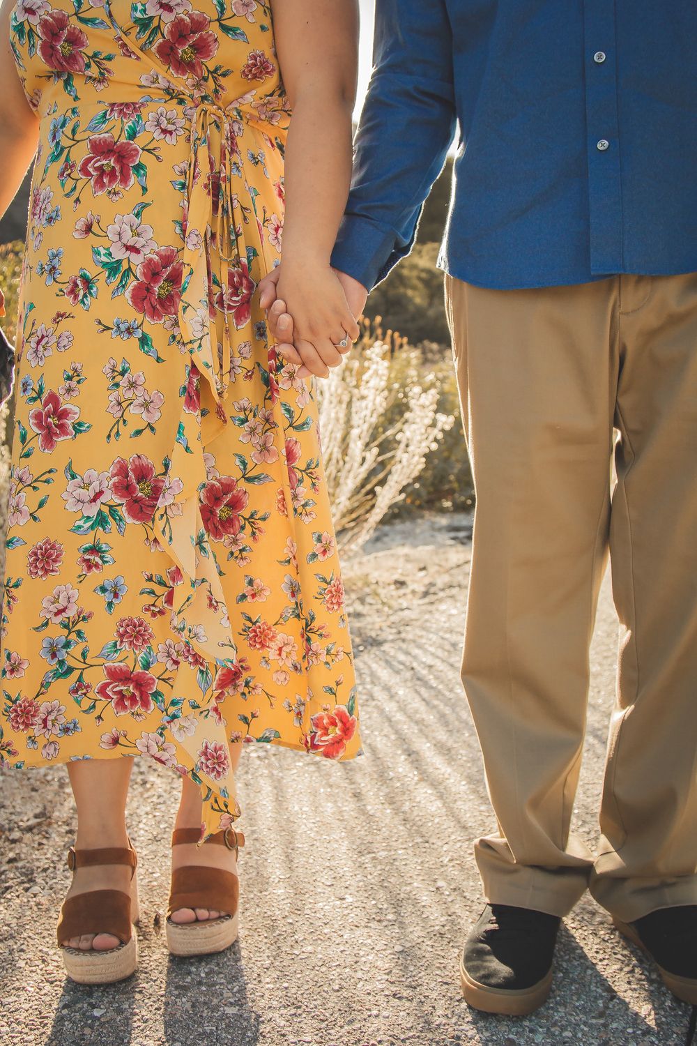 Close-up of couple's hands holding while wearing yellow floral dress and blue shirt with khaki pants.