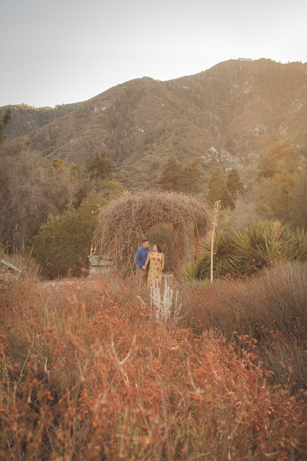Distant view of couple standing under natural arch with mountains in background.