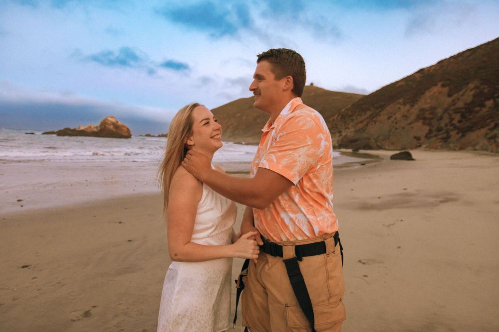 Tender moment shared on sandy beach with coastal cliffs and ocean views.
