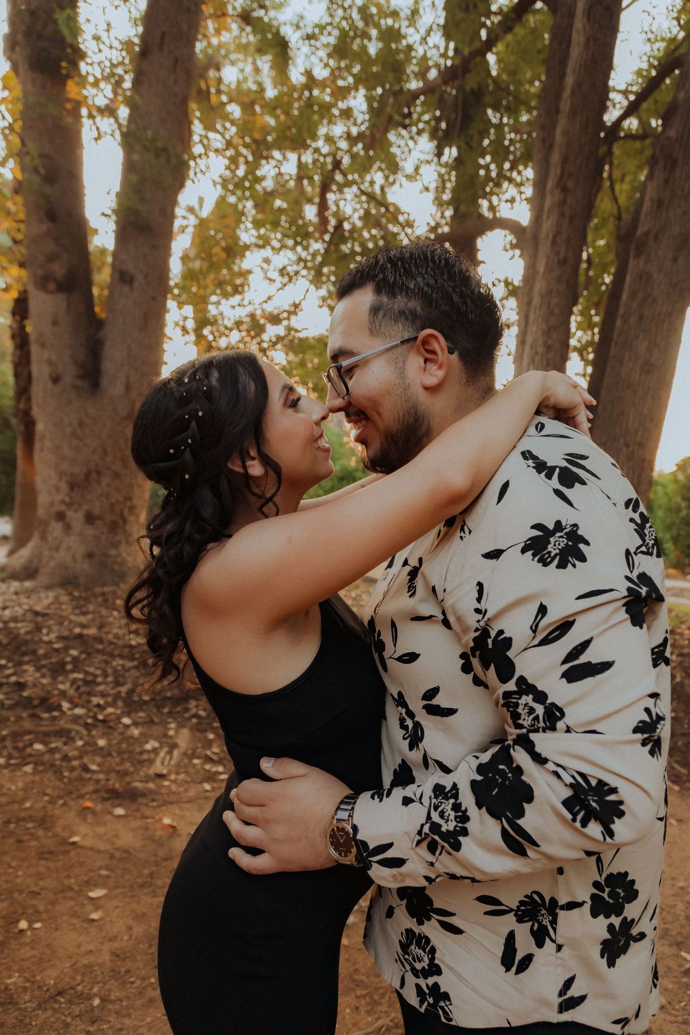 Intimate couple moment captured in golden hour light among tall trees.