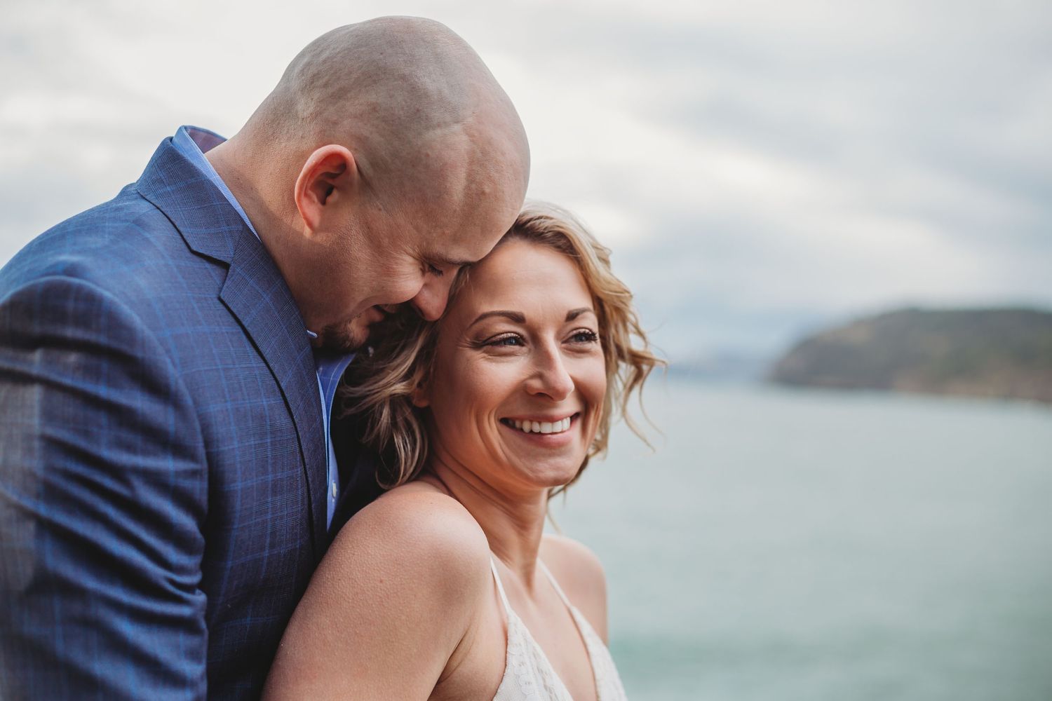A groom stands behind his new bride at their beach elopement.